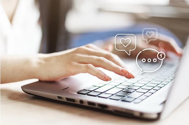 A person typing on a laptop keyboard with illustrated chat and notification icons, including hearts and message bubbles, appearing above the keys.