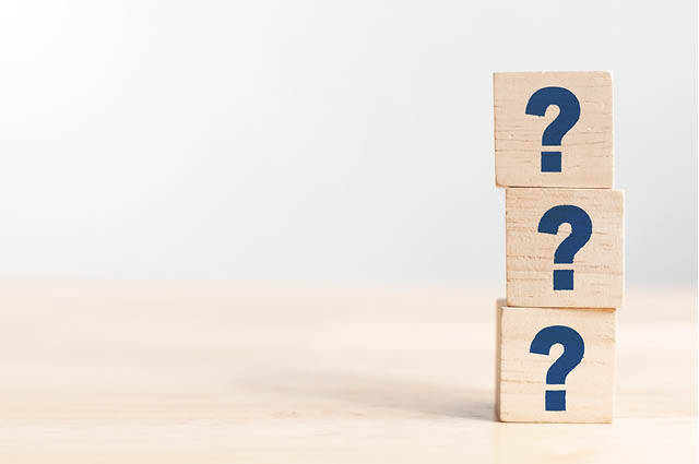 Three wooden blocks stacked vertically, each displaying a blue question mark, sit on a light wooden surface against a plain, light background.