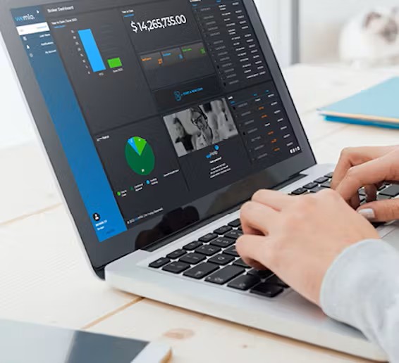 A person types on a laptop displaying a financial dashboard with charts and graphs, including a bar graph, pie chart, and monetary values, on a bright desk with documents nearby. A person types on a laptop displaying a financial dashboard with charts and graphs, including a bar graph, pie chart, and monetary values, on a bright desk with documents nearby.