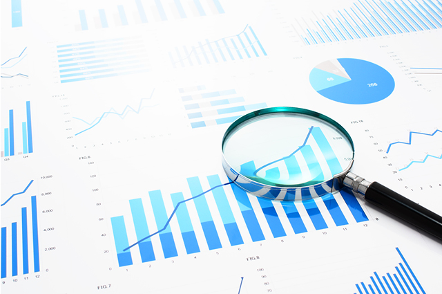 A magnifying glass lies on printed financial charts and graphs with blue bars and lines, emphasizing data analysis and business growth. Pie charts and line graphs are also visible in the background.