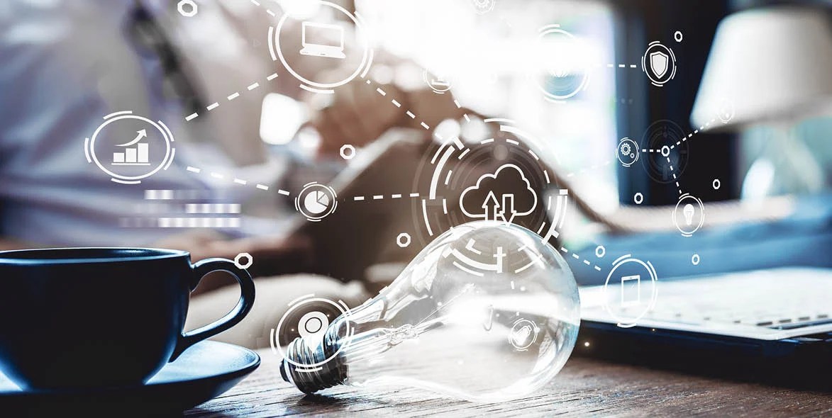 A close-up of a light bulb on a desk near a coffee cup and laptop, with digital technology and cloud computing icons superimposed, suggesting innovation and brainstorming. A close-up of a light bulb on a desk near a coffee cup and laptop, with digital technology and cloud computing icons superimposed, suggesting innovation and brainstorming.