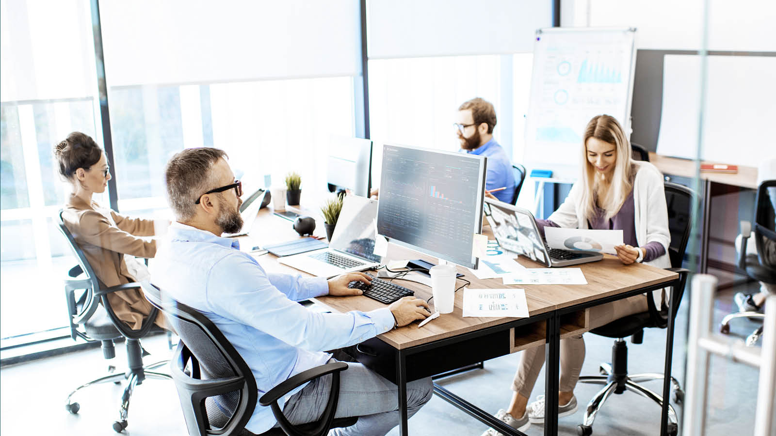 four people working on computers at a table, representing the productivity achieved when outsourcing support