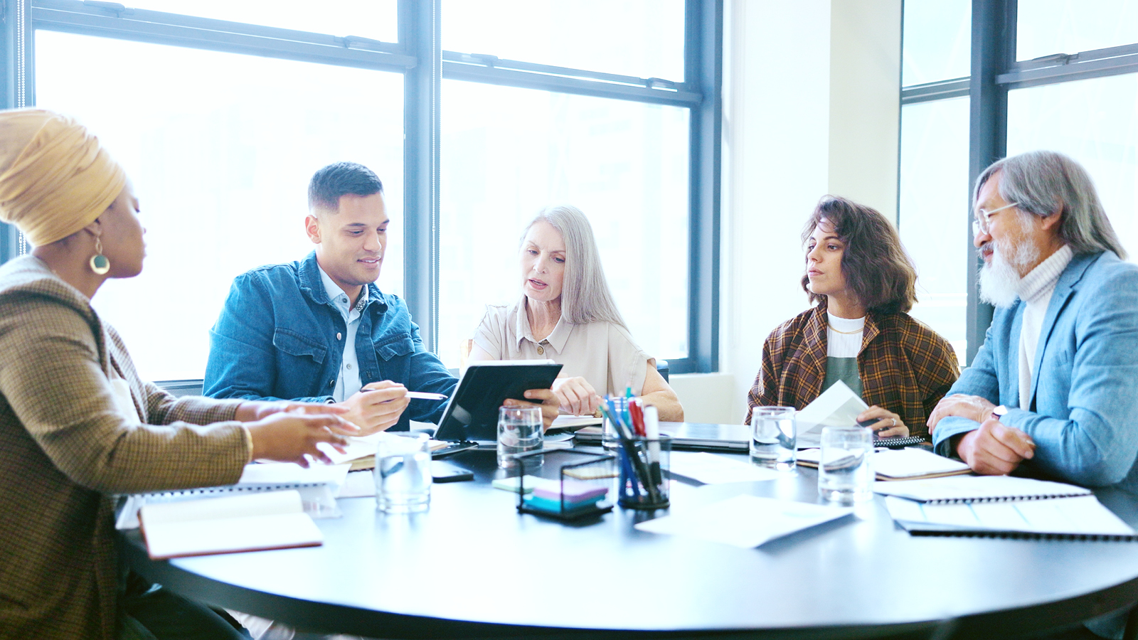 A group of professionals seated around a conference table reviewing documents and a tablet during a collaborative discussion about borrower and lending solutions.